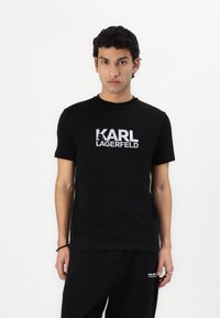 Μαύρο βαμβακερό μπλουζάκι με έντονο λευκό λογότυπο "KARL LAGERFELD", στρογγυλή λαιμόκοψη, κοντά μανίκια και χαλαρή εφαρμογή.