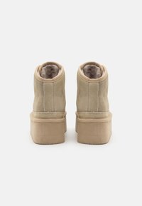 Stivaletti alla caviglia in suede beige con imbottitura interna morbida, forma arrotondata e suola più spessa. Texture liscia con dettagli di cucitura discreti.