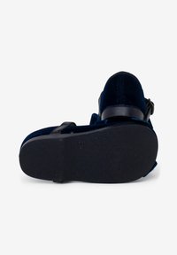 Sandalia de terciopelo azul marino con hebilla ajustable negra, suela texturizada y diseño de espalda abierta, con bordes suaves y patrones mínimos.