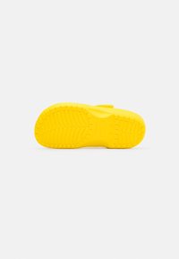 Yellow footwear with a textured, non-slip sole and a curved shape. Features a strap for secure fit. Smooth material with a bright finish.