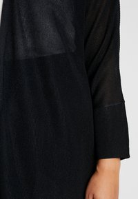 Černý, lehký pletený kardigan s texturovanou, průsvitnou horní částí a dlouhými rukávy. Výrazné žebrované manžety dodávají designu detail.