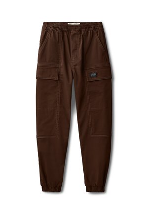 Veste noire zippée avec poignets élastiques, associée à un pantalon cargo marron avec poches et chevilles élastiques. Baskets blanches avec accents de logo.