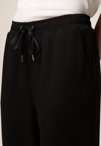 Schwarze Jogginghosen mit elastischem Bund, satinierter Kordelzug und tonal gesticktem "SOFT LIFE"-Schriftzug an der Seite. Weiche Stofftextur.
