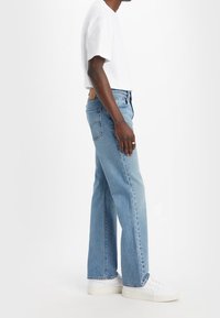 Jeans de denim azul claro con corte recto, combinados con una camiseta blanca de manga corta y zapatillas blancas. Presentan un bolsillo trasero.