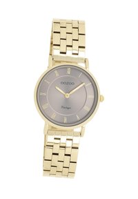 Montre dorée avec un bracelet métallique, cadran gris rond, chiffres romains et texte subtil indiquant "OOZOO Vintage". Fini lisse et poli.