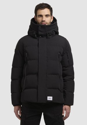 Sort pufferjakke med høj krave, lynlåslommer og kviltet design. Har et mærke på den nederste søm og justerbare snore.
