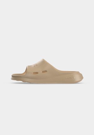 Sandale beige à enfiler avec une tige fermée, des trous de ventilation sur le côté et une semelle texturée marquée "Lacoste."