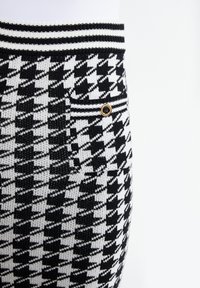 Kalhoty s černobílým vzorem houndstooth vyrobené z pletené látky, s detailním zlatým knoflíkem na kapse a žebrovaným páskem.