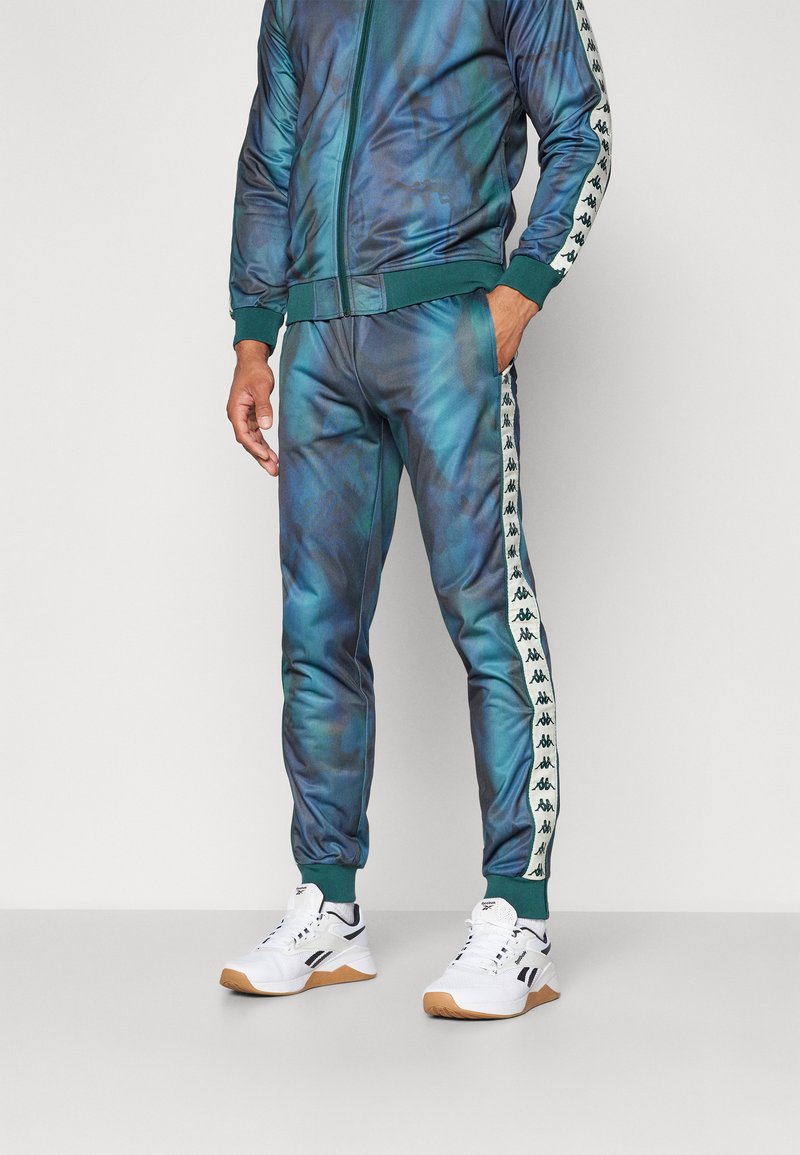 Chándal en un degradado azul-verde, con chaqueta de cremallera y pantalones ajustados con franjas laterales y logotipos blancos. Tejido suave y ligero.