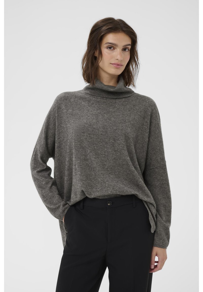 Gaiši pelēks, brīvi pieguļošs džemperis ar augstu, sarullētu izgriezumu, izgatavots no mīkstas auduma, ar sānu spraugām un garām piedurknēm, apvienots ar melnām biksēm.