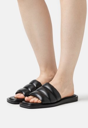 Black leather slide sandals featuring wide padded straps, open toe design, and a flat rubber sole. Smooth texture and minimalistic design.