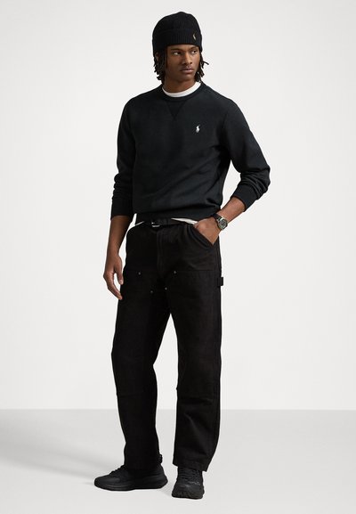 Sort sweatshirt med rund halsudskæring, hvide detaljer, parret med sorte løstsiddende bukser med lommer. En sort beanie og sneakers fuldender looket.