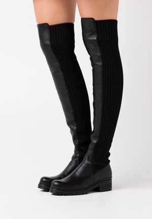 Botas negras hasta los muslos con parte superior de punto acanalado y parte inferior de cuero suave, que presentan una suela gruesa y sin herrajes visibles.