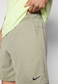 Ανδρικές μπεζ αθλητικές βερμούδες με ελαστική μέση, απαλή υφή, δύο πλαϊνές τσέπες και μικρό μαύρο λογότυπο Nike στο κάτω μέρος.