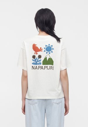 Person mit kurzen schwarzen Haaren, die ein weißes T-Shirt mit bunten Grafiken von Vogel, Sonne, Blume und Berg sowie dem Text "NAPAPIJRI" auf der Rückseite trägt.