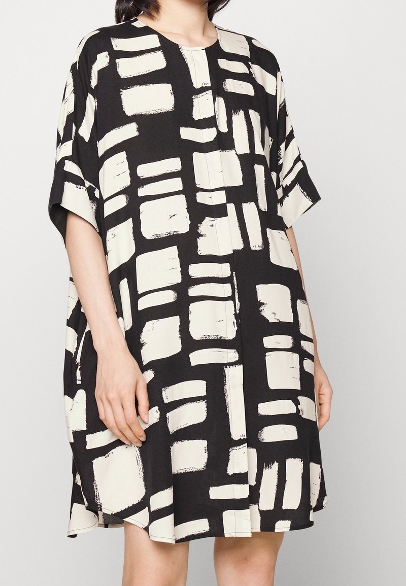 Svart och vit knälång klänning med abstrakt penselmönster, korta ärmar och rund halsringning. Tillverkad av lättviktigt tyg.