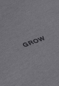 Tissu gris avec le mot "GROW" imprimé en lettres majuscules noires, centré et légèrement incliné.