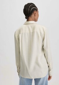 Cremfarbene Langarmbluse mit Kentkragen, Rückeneinsatzdetail und Knöpfen an den Manschetten, kombiniert mit hellblauen Jeans. Glattes, leichtes Material.