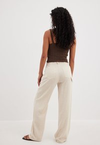 Gai bēšas plašās bikses apvienotas ar teksturētu brūnu austu augšu, kurai ir aizmugurējās kabatas un brīvas formas dizains komfortam.