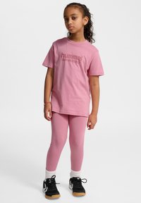 Pink Hummel t-shirt med logo, parret med matchende pink leggings. Skoene er sorte med hvide detaljer og lyse såler.