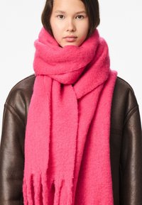 Lyserødt uld tørklæde med blød tekstur og frynser i enderne, viklet om halsen og kombineret med en mørkebrun læderjakke.