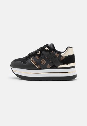 Schwarzer Plateau-Sneaker mit braunen Logo-Mustern, goldenen Akzenten, dicker weißer und schwarzer Sohle sowie schwarzen Schnürsenkeln auf schlichtem weißem Hintergrund.