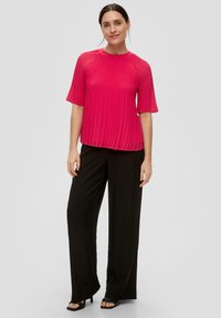 Magenta geplooid top met korte mouwen, ronde halslijn en een vloeiende ontwerp, gecombineerd met zwarte wijde broek en openteen zwarte hakken.