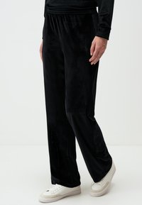Pantaloni di velluto nero con un taglio rilassato, dotati di un elastico in vita. Texture liscia e gambe dritte, abbinati a sneakers bianche.
