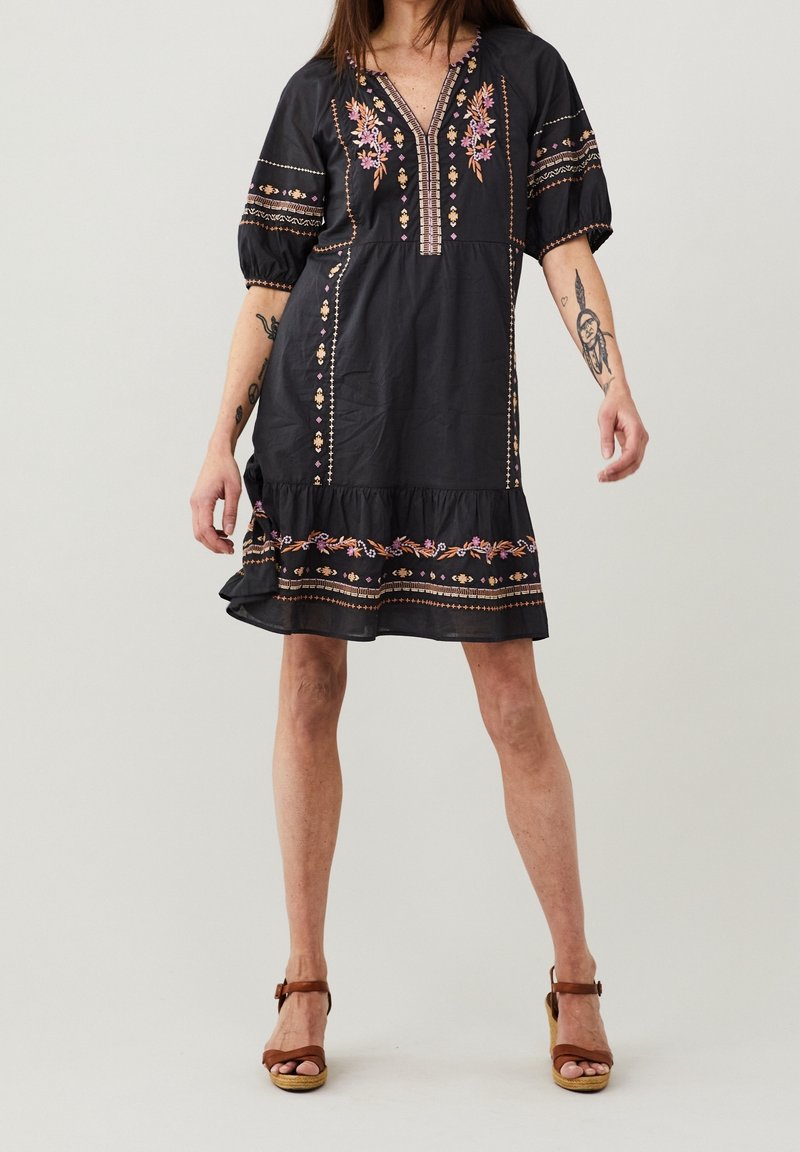 Robe en coton noir avec broderies florales, manches courtes et ourlet volanté à étages. Présente un décolleté en V profond et des motifs de couture décoratifs.