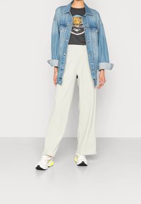 Denim jacket, gray graphic tee with tiger print, light green wide-leg pants, and white sneakers with yellow accents.
