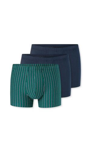 Homme torse nu aux cheveux bruns courts portant un boxer rayé vertical vert et noir, debout devant un fond clair uni.