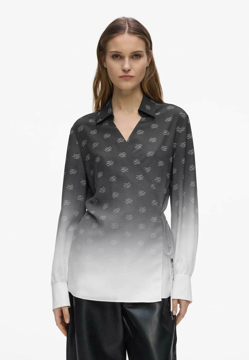 Femme portant un chemisier à manches longues avec un dégradé du noir au blanc et de petits motifs de logos blancs, ainsi qu'un pantalon noir à jambes larges.