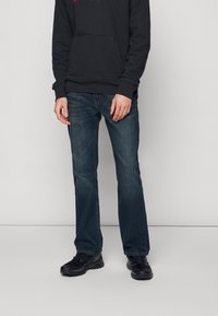 Jeans de mezclilla oscura con un diseño de pierna recta, combinados con una sudadera negra que presenta un logo rosa y zapatillas deportivas negras. Textura suave.