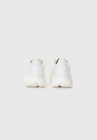 Baskets de sport blanches avec une tige en mesh texturé, un col rembourré et une semelle épaisse, présentant un design minimaliste et des accents doux et lisses.
