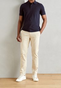 Marineblauwe poloshirt met korte mouwen, crèmekleurige chinos en witte sneakers. Gladde katoenstructuur, klassieke snit en subtiele logo op de polo.