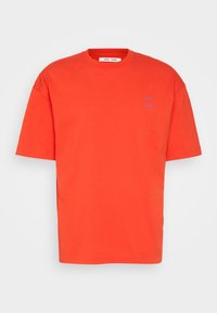 T-shirt orange à manches courtes en coton, avec un col rond et un petit logo violet sur la poitrine gauche. Design simple et coupe décontractée.