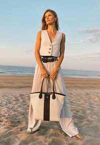 Grand sac fourre-tout structuré en matériau tissé crème avec une base et des accents en cuir noir. Il dispose de poignées noires robustes et d'une fermeture supérieure.