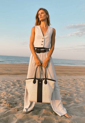 Grand sac fourre-tout structuré en matériau tissé crème avec une base et des accents en cuir noir. Il dispose de poignées noires robustes et d'une fermeture supérieure.