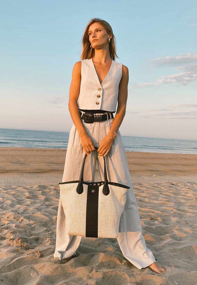 Grand sac fourre-tout structuré en matériau tissé crème avec une base et des accents en cuir noir. Il dispose de poignées noires robustes et d'une fermeture supérieure.
