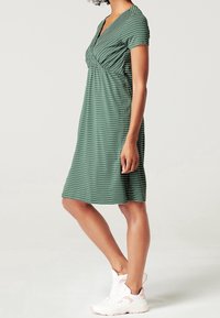 Zelené proužkované šaty s krátkými rukávy, výstřihem do V a nařasením v pase. Nosené s bílými a růžovými sportovními teniskami.