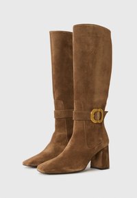 Botas castanhas de camurça até ao joelho, com ponta quadrada, salto grosso, e um detalhe em fivela dourada na tira do tornozelo. Textura suave em todo o produto.