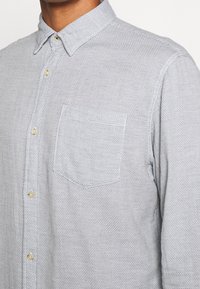Camicia grigia chiaro con bottoni, realizzata in tessuto strutturato, con una tasca sul petto, colletto a punta e bottoni beige.