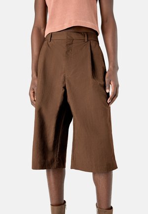 Shorts marrones de pierna ancha hechos de un tejido ligero, con una cintura alta y pliegues frontales. La textura es suave y cuenta con bolsillos laterales.