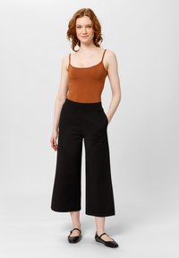 Brązowy dopasowany top na ramiączkach w zestawieniu z czarnymi spodniami o szerokich nogawkach. Całość charakteryzuje się gładką strukturą oraz minimalistycznym wzornictwem bez widocznych wzorów.
