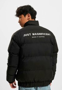 Jachetă puffer neagră cu guler înalt, având textul alb "DOAR MAGNIFIC" pe spate. Design texturat, cu capitonaj.