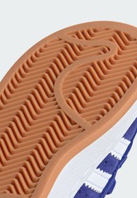 Semelle de chaussure avec un fond en caoutchouc texturé orange, avec un motif en vagues ; accents blancs sur les côtés et une partie supérieure bleu foncé.