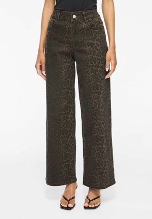 Kvinde iført højtaljede bukser med vide ben med mørkebrun leopardprint og sorte sandaler, stående mod en hvid baggrund.
