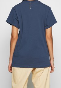 Náměsíčná modrá bavlněná tričko s krátkými rukávy, hladkou texturou a rovnými liniemi. Obsahuje krátký zip na zadní straně.