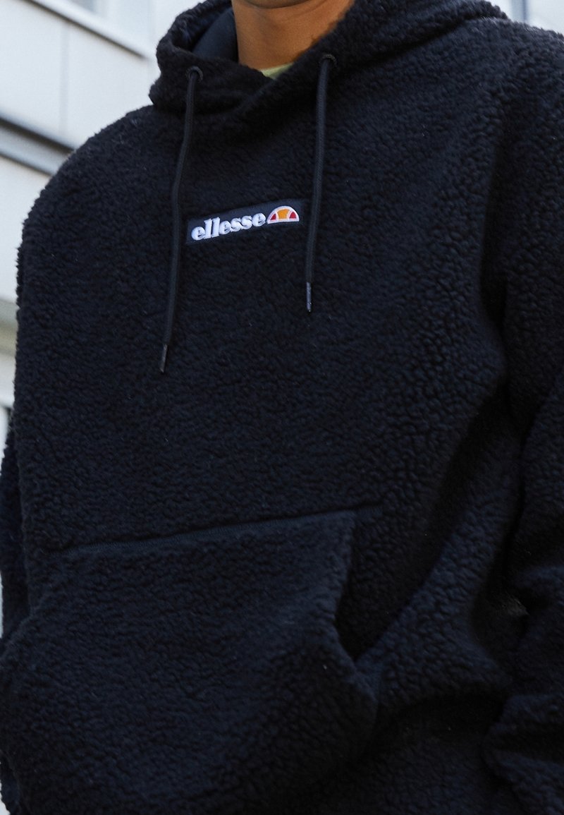 Felpa nera con cappuccio in pile, tasca a marsupio, cappuccio con coulisse regolabile e logo bianco sul petto con accenti rossi e gialli.