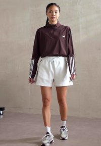 Bordo ilgos rankovės marškiniai su balta adidas logotipu, derinami su baltais elastingais šortais su juodais akcentais ir baltais kojiniais bei sportbačiais.